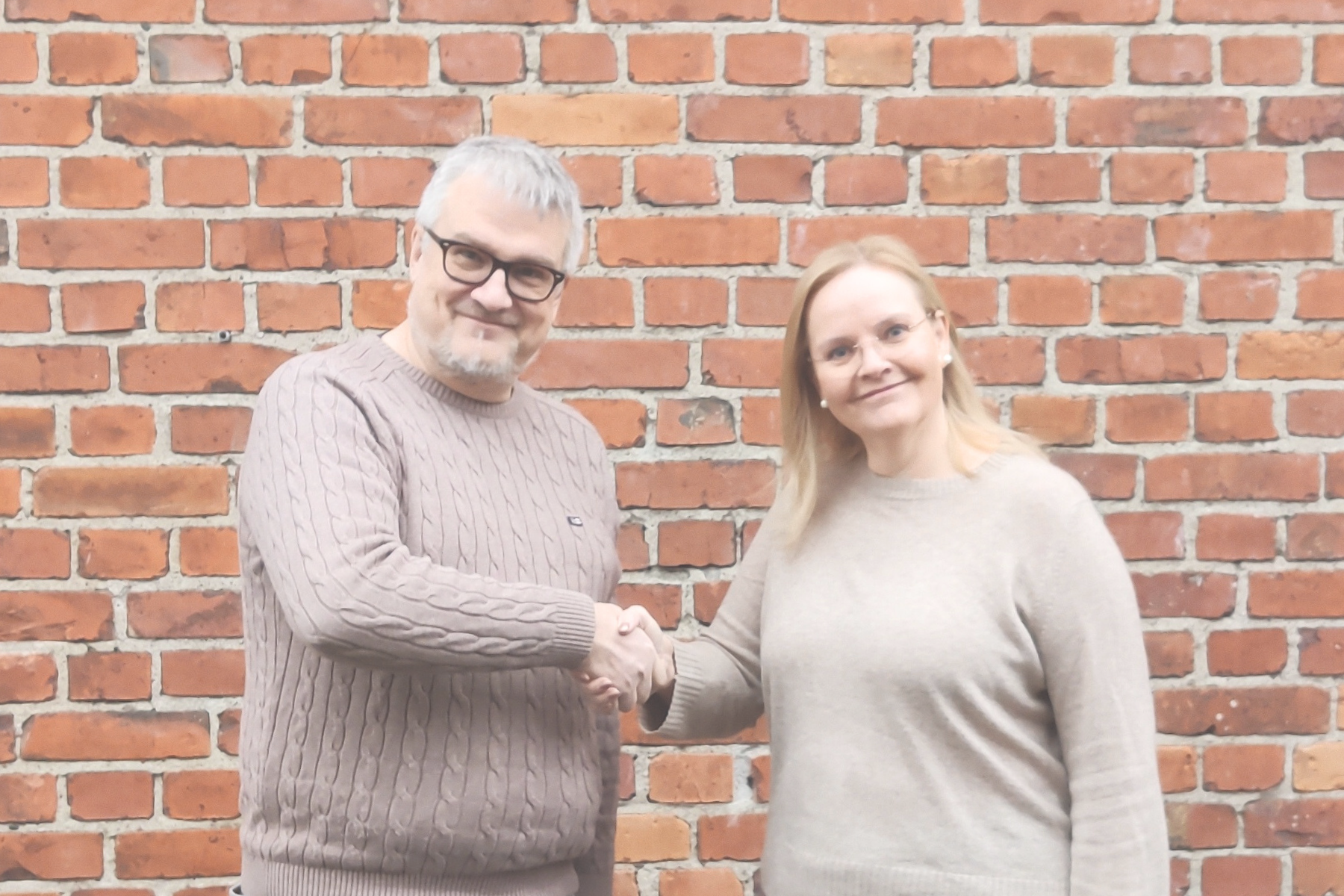 Mika Ollikainen ja Maija Karhusaari kättelevät tiiliseinän edessä